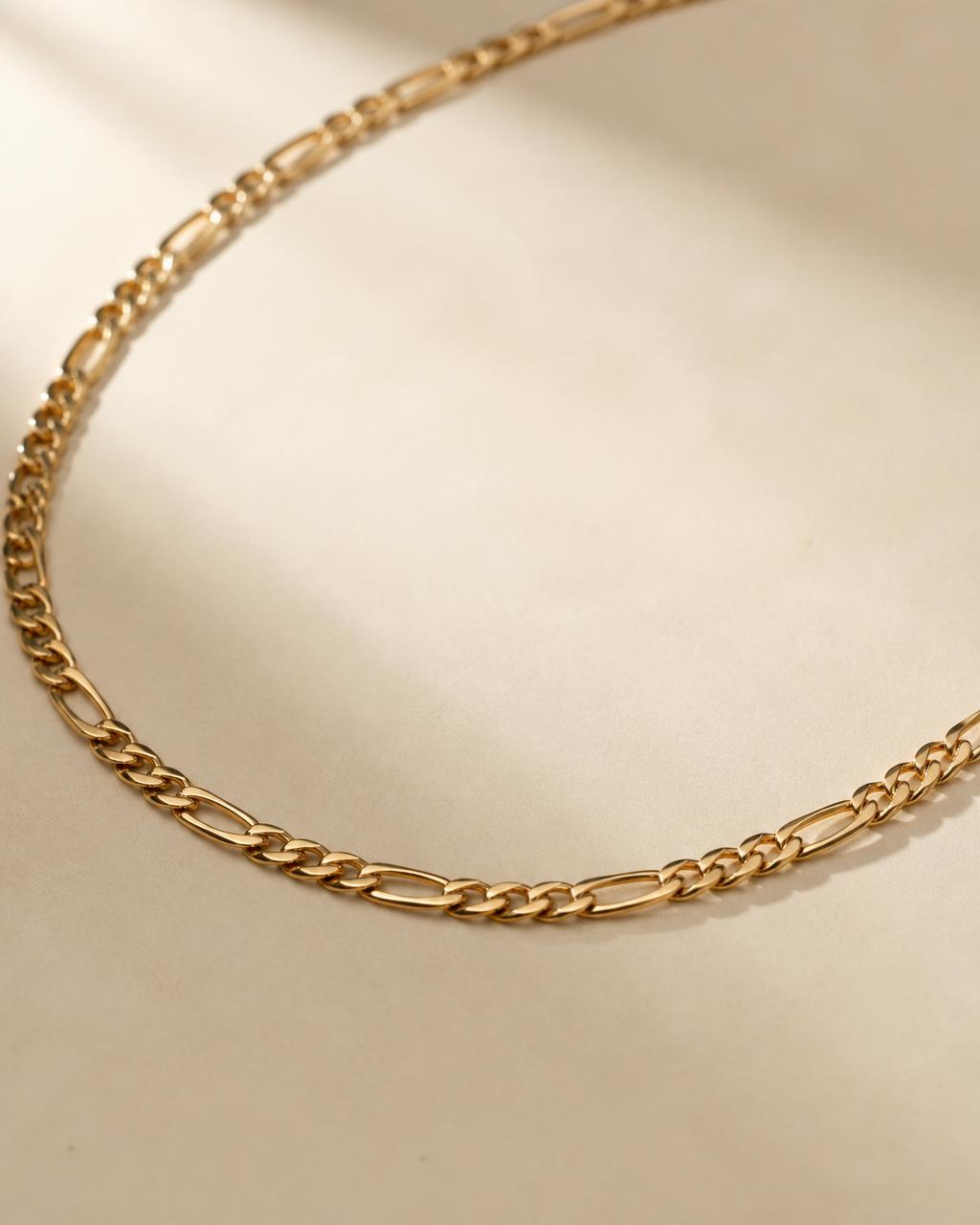 Solid gold Figaro link chain laid across dark slate